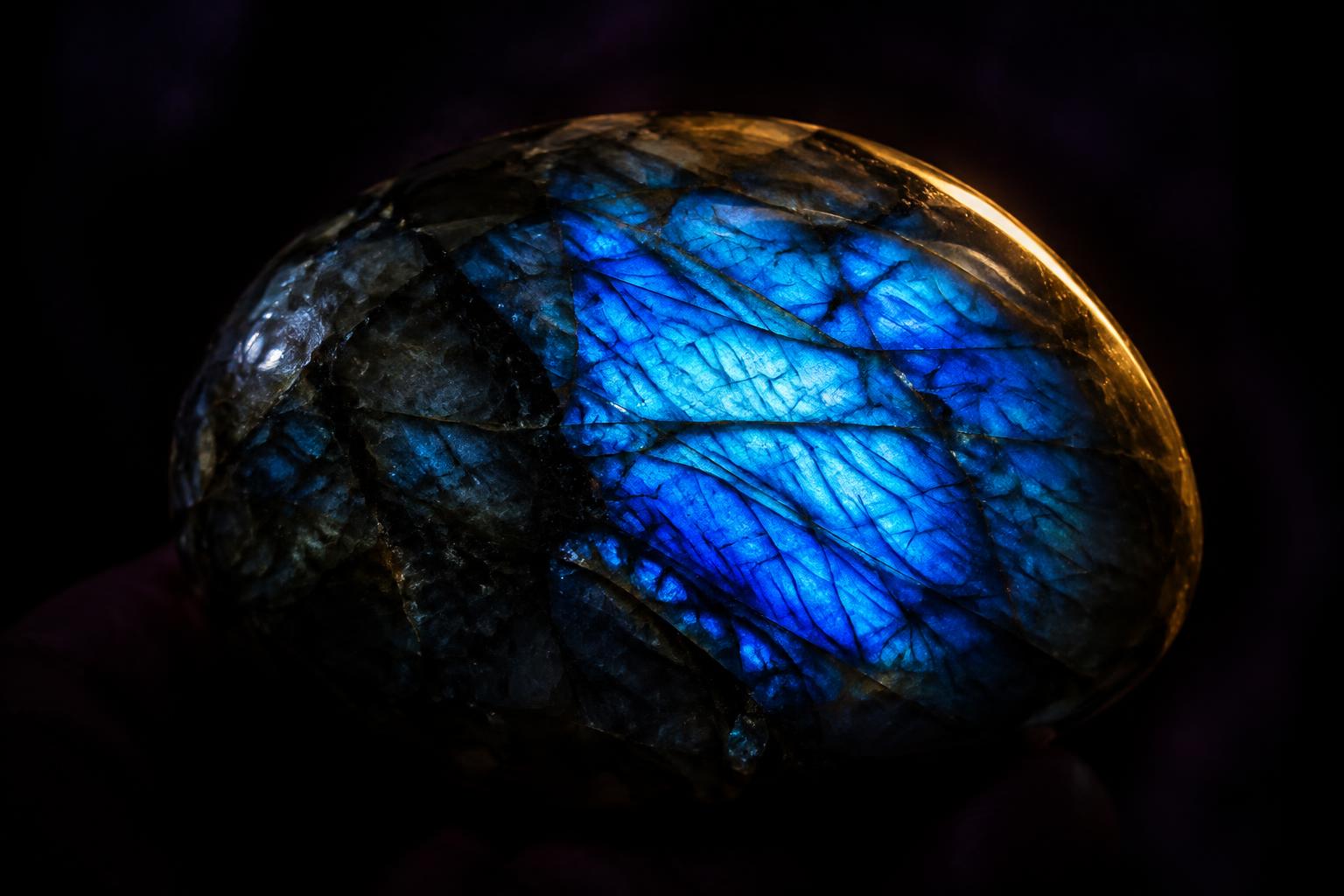 A polished labradorite stone flashing blue and gold across its whole face, on dark cloth